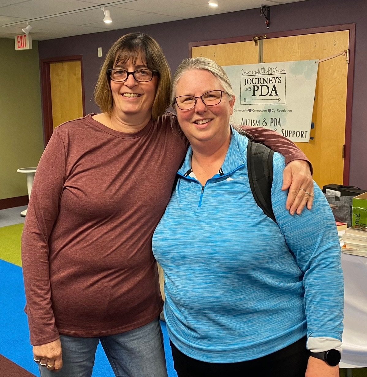Two attendees embracing in front of the Journeys With PDA banner